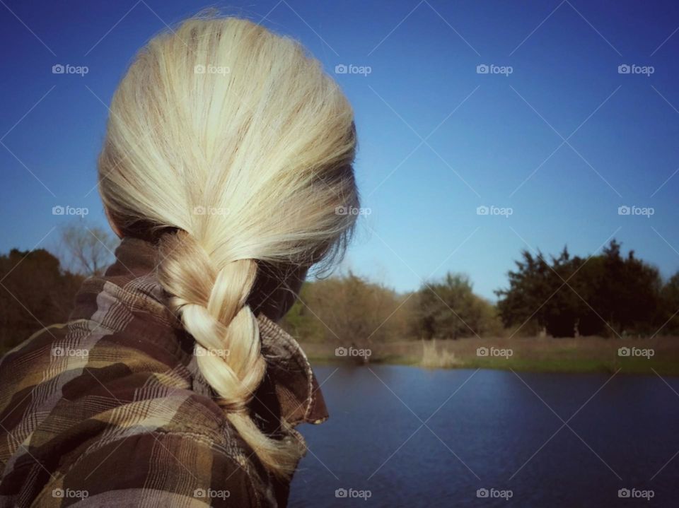 Woman with a blond braid from the back looking at a pond in winter