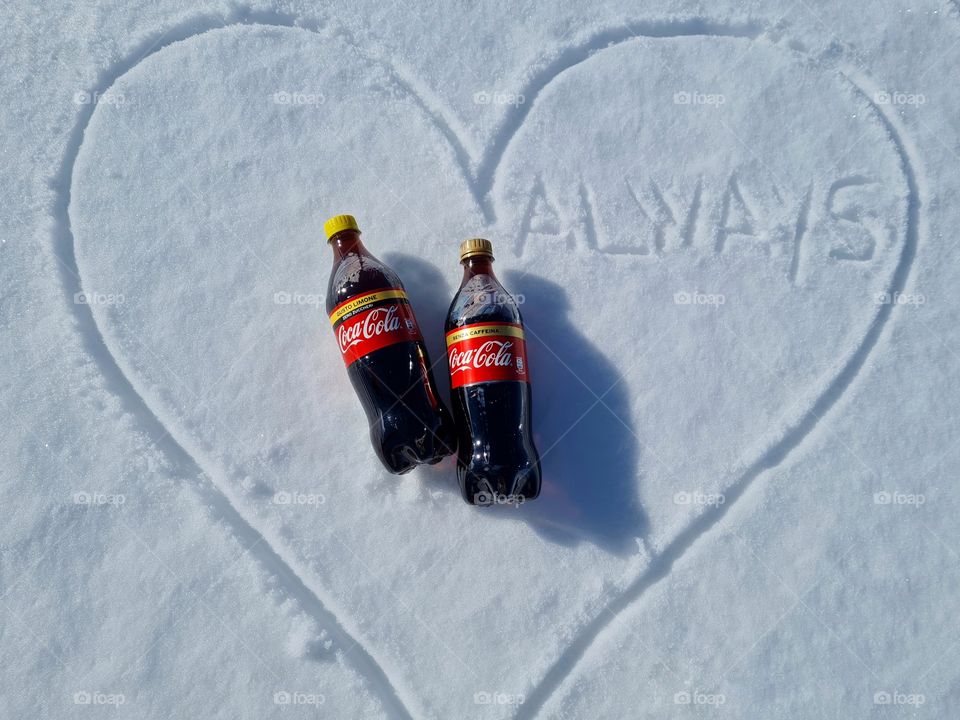 bottles of Coca Cola resting on the snow and written always