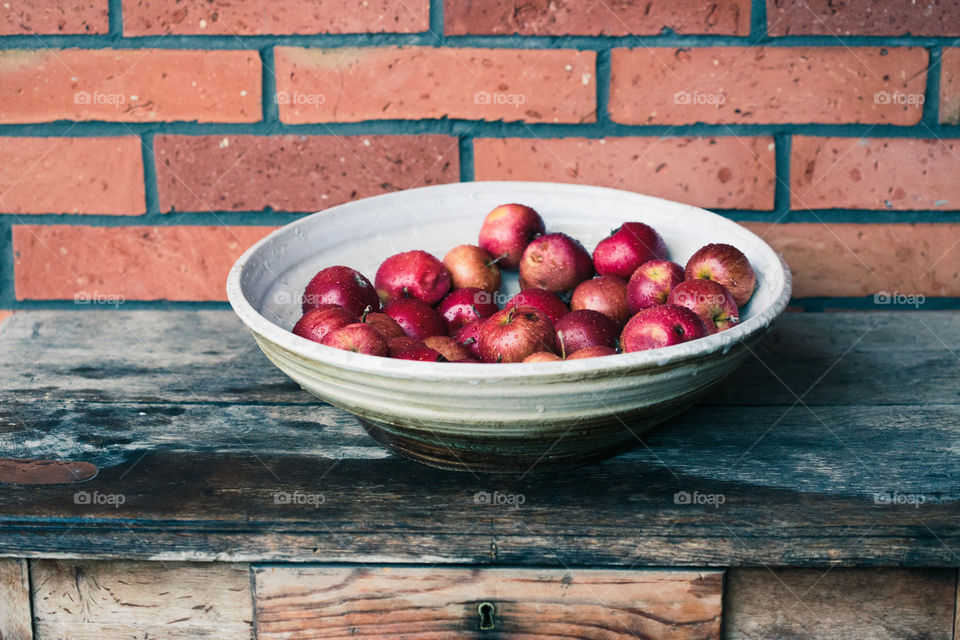 Closeup of big bowl of fresh red apples sprinkled raindrops on wooden table