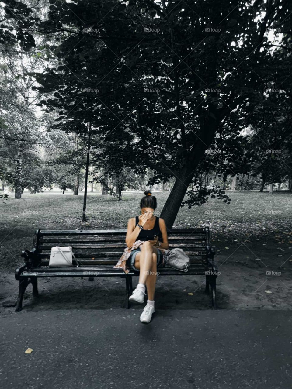 Evening. Park. The girl sits on a wooden bench in the park and carefully looks into the phone