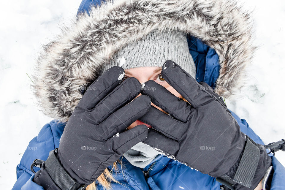 Millennial girl dressed for winter and covering her face with gloved hands outdoors in the snow