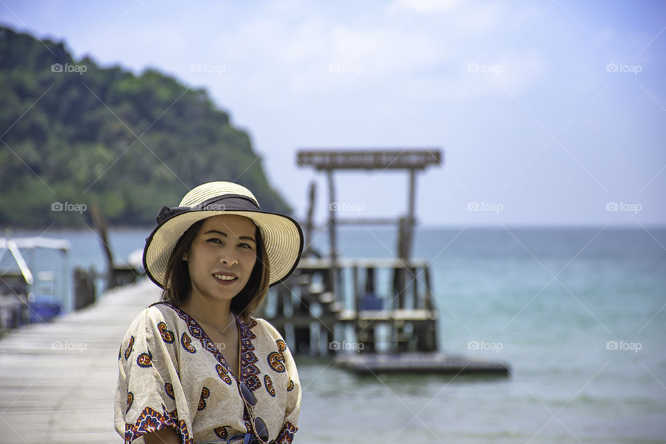 Women Wear a hat on the wooden bridge pier boat in the sea and the bright sky at Koh Kood, Trat in Thailand.