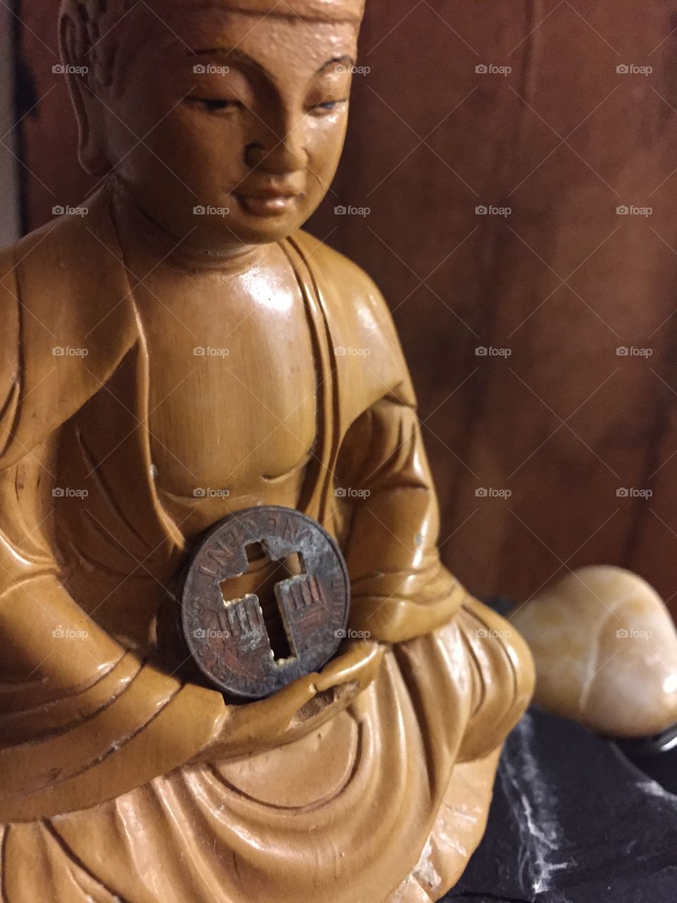 Buddha and Penny Cross. A closeup of a Buddha figurine with penny that has cutout cross in lap on top of a fountain. 