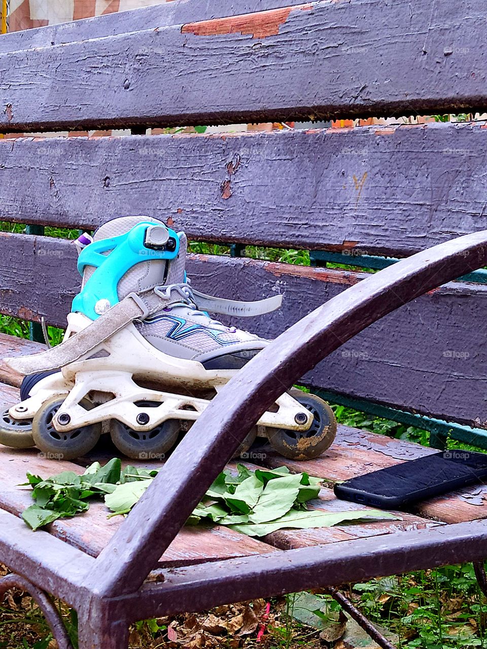 An old wooden bench on which  green roller skates, a tree branch with green leaves and a black telephone