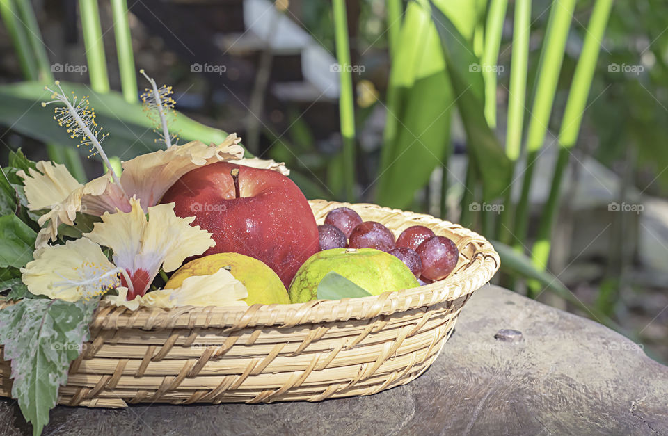 Apple, Orange and grape in weave bamboo baskets with floral decorations Background blurry trees.