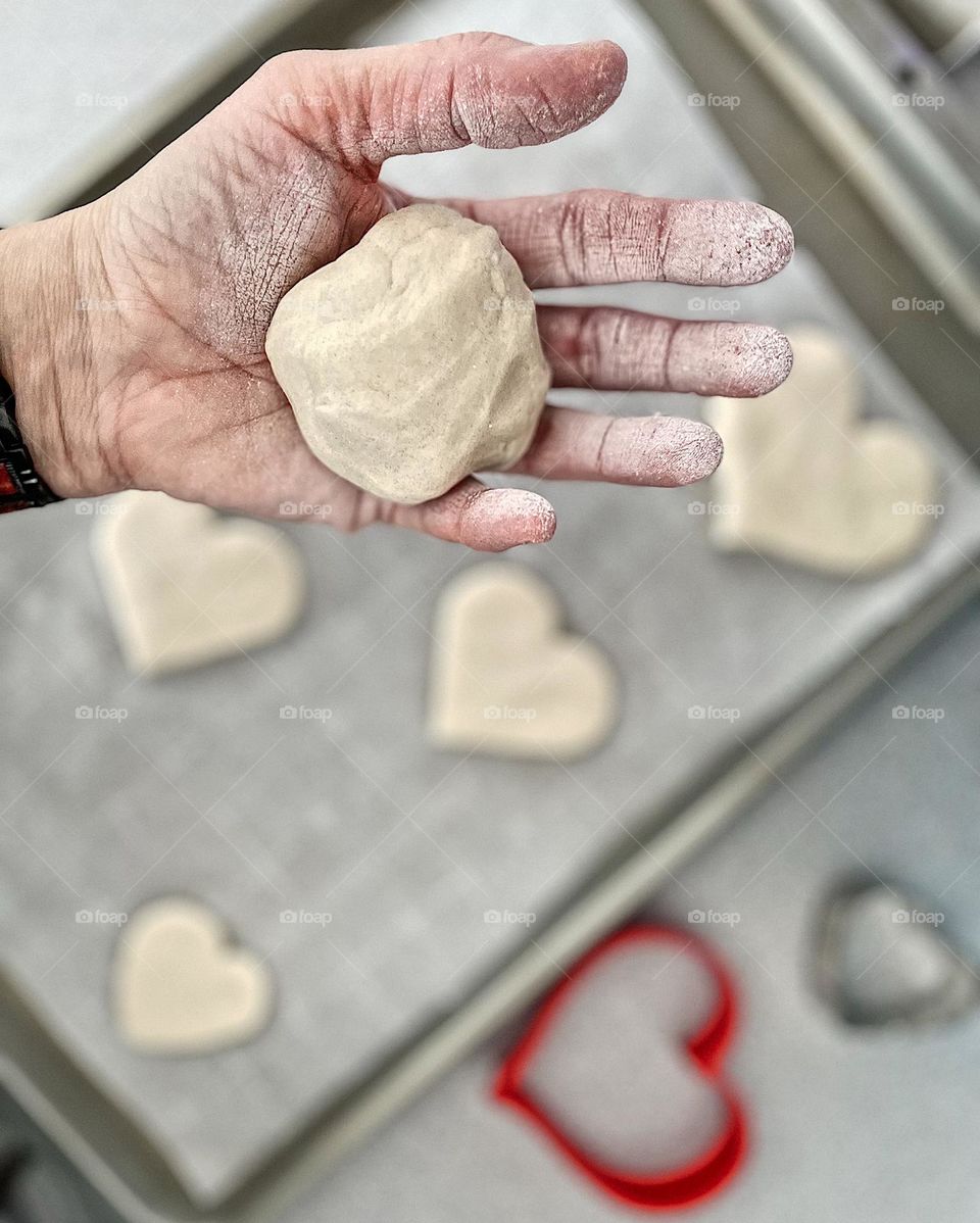 Woman’s hand holds dough, making hearts from dough, woman uses white dough, baking at home, woman’s hands getting dirty in the kitchen