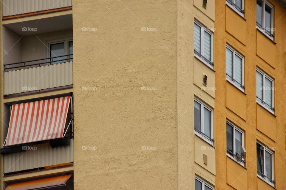 Full frame shot of a tall yellow house with many windows and balcony with awning