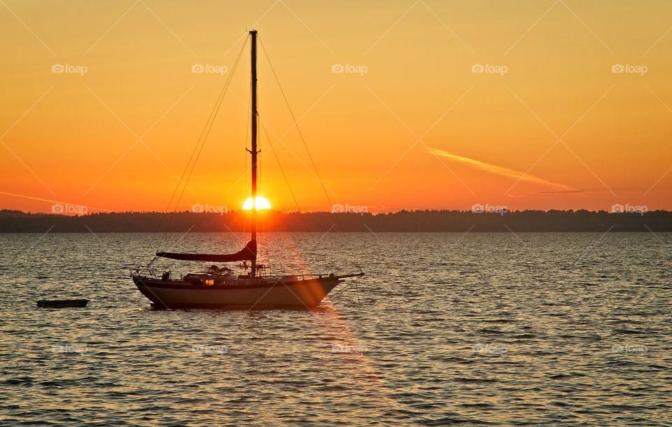 The sun sets behind a sailboat