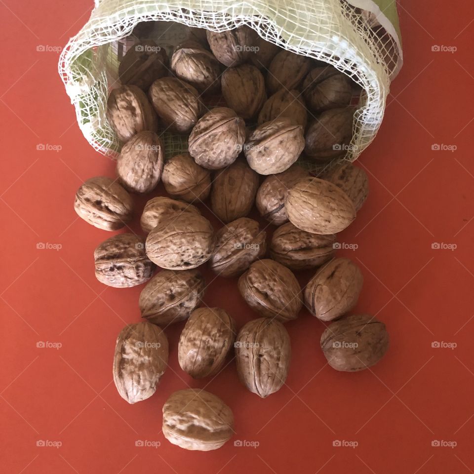 Hole walnuts in open mesh bag on orange table