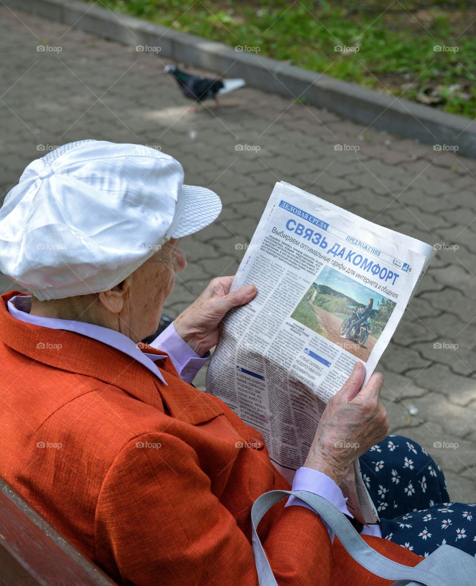 old woman reading press on a street bench