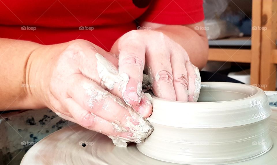 two hands creating a clay pot