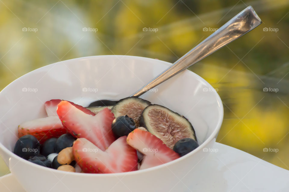 Fresh fruit and yogurt smoothie bowl outdoors with heart shaped strawberry, blueberry, fig and cashews and almond with honey on top closeup healthy lifestyle antioxidant background