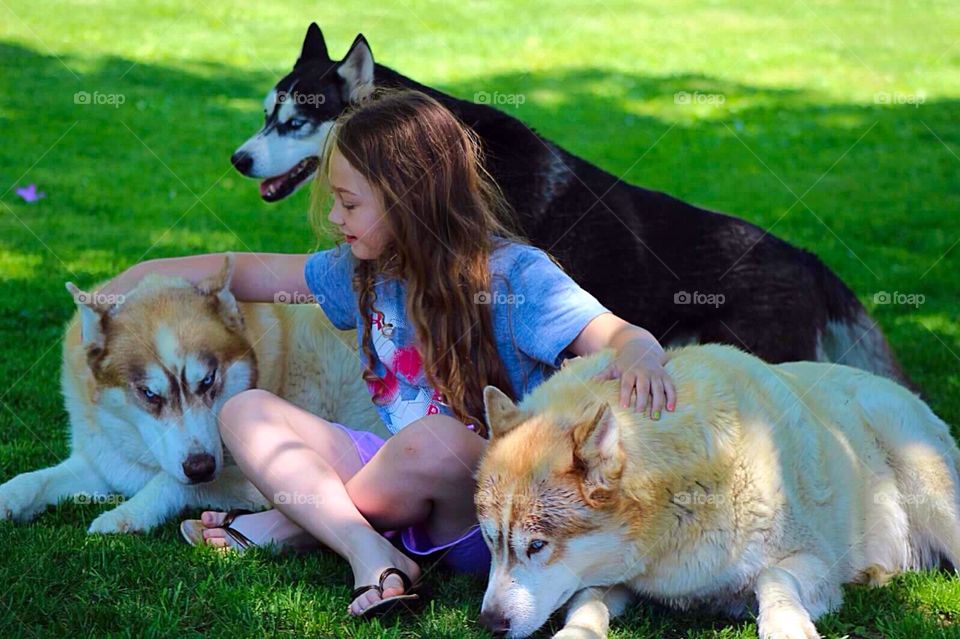 Close-up of girl sitting with dogs on green grass