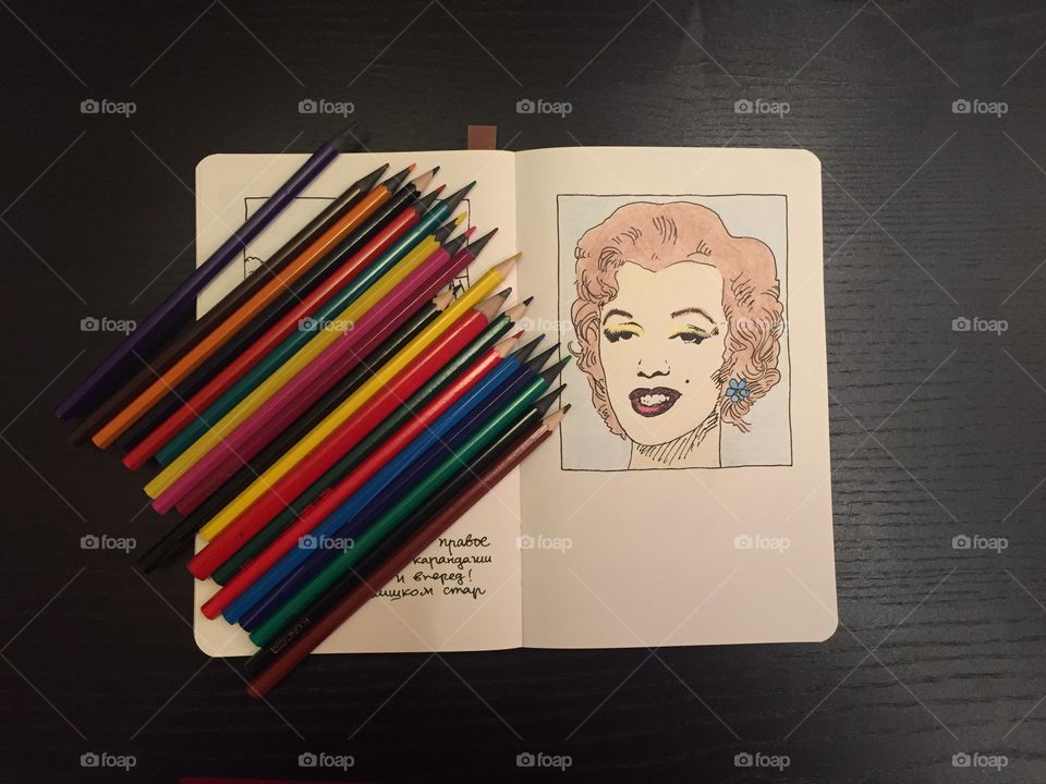 Colored pencils and a drowning in a book on a black table