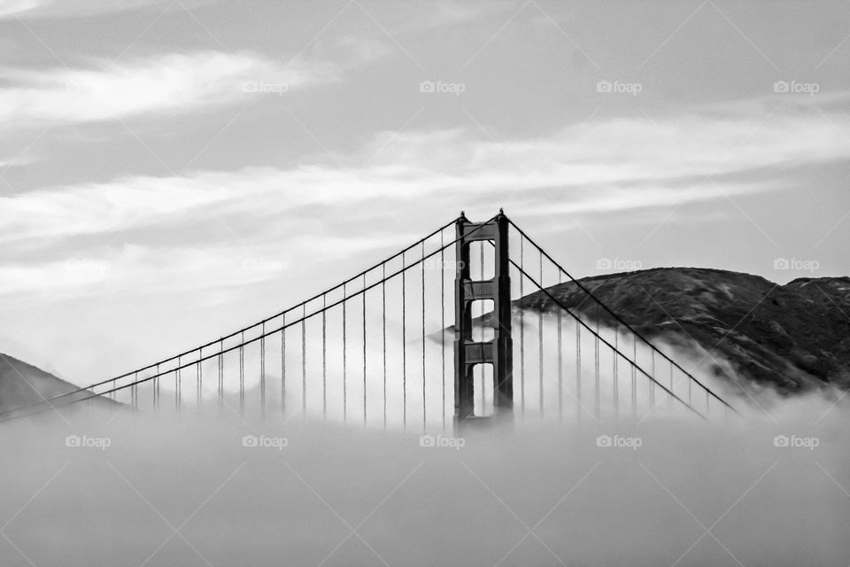 Black and white image of the Golden Gate Bridge peeking through the fog in San Francisco California 