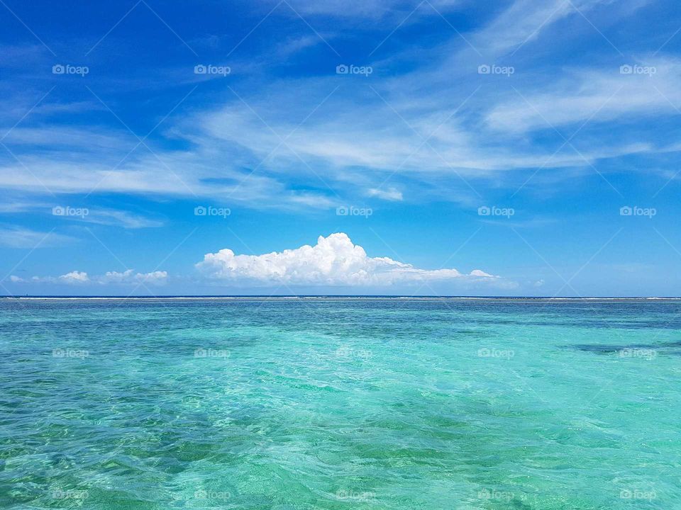Turquoise Caribbean Sea with a white cloud on a clear blue sky