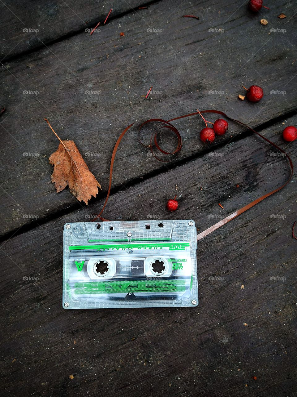 Nostalgia.  On a wooden table lie: a cassette tape with brown tape, red berries and an autumn leaf