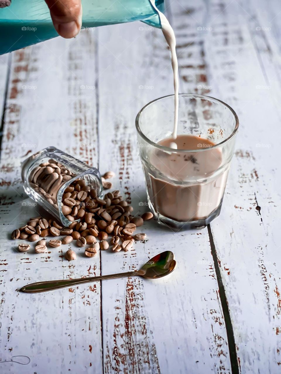 A cup of milk coffee with spill coffee beans on a white wooden top
