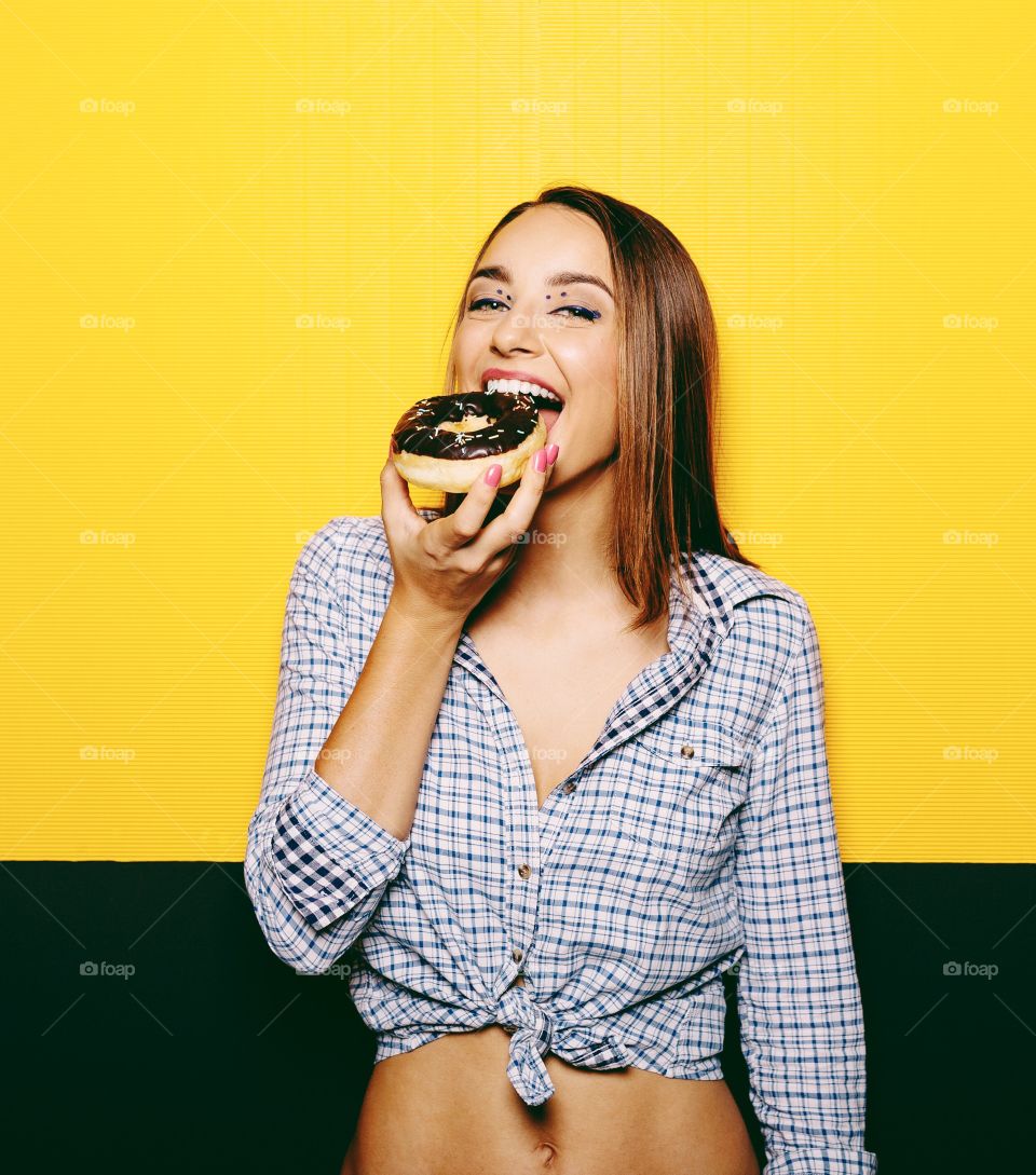 Sweet donut . Girl eating donut with chocolate icing on yellow background