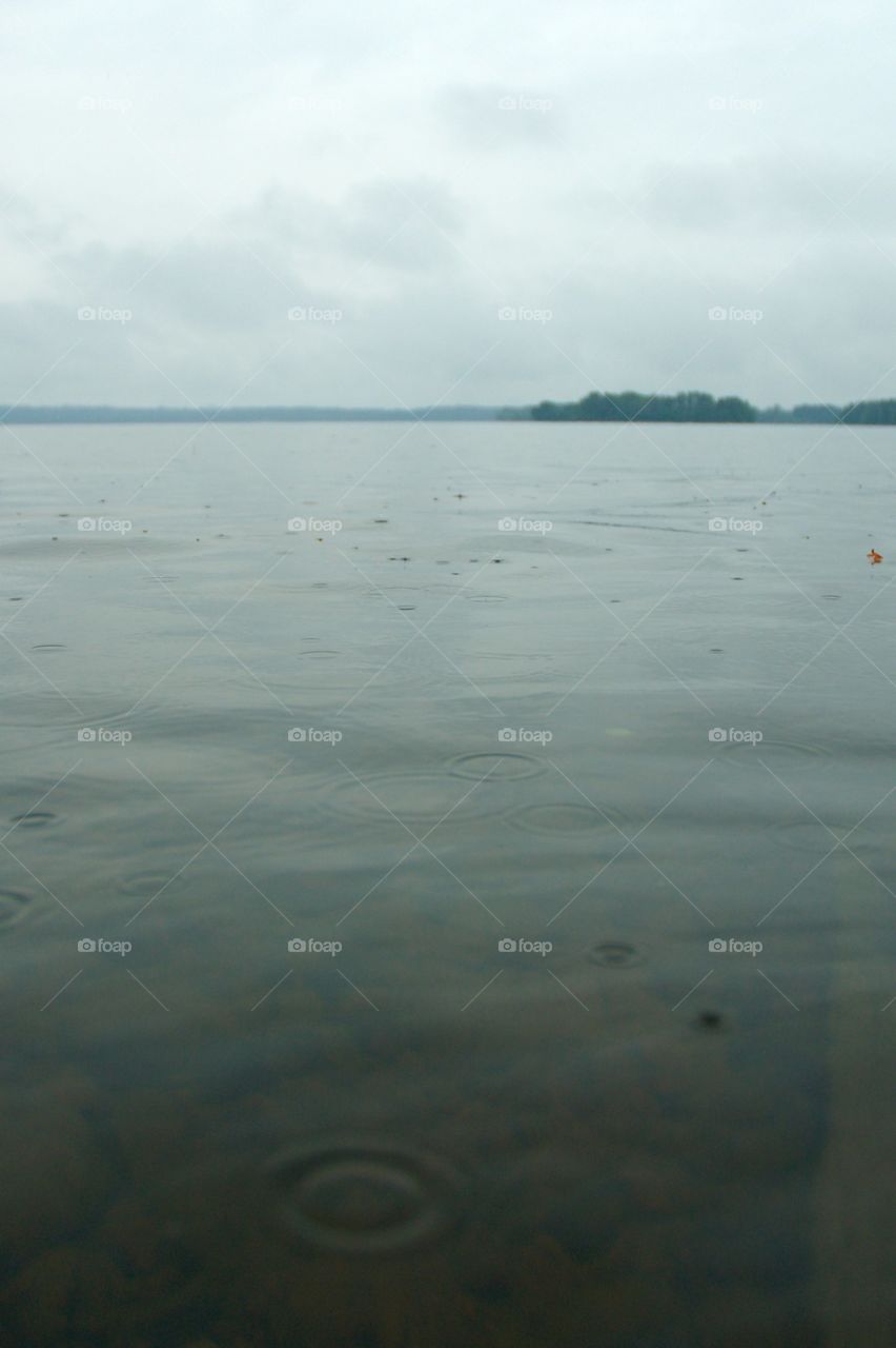 Raindrops falling on the surface of a lake, with an island in the background.