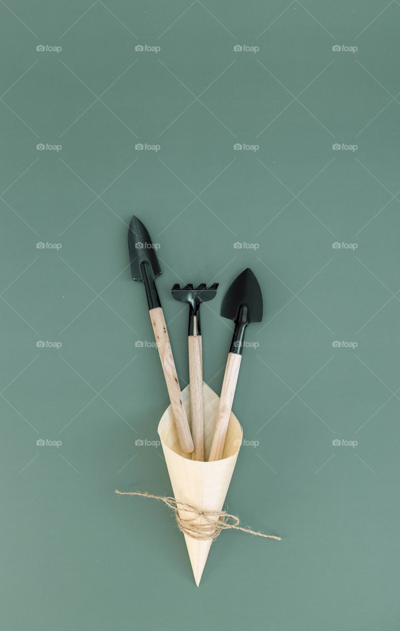 Three garden tools in a wooden cone tied with jute thread in a bow lie on a natural green background fdat ley close-up.