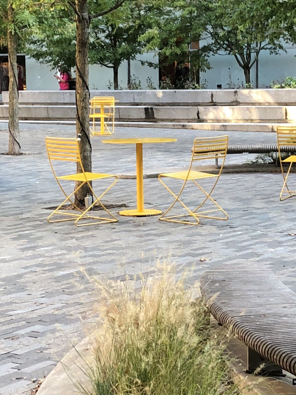 Yellow metal table and chairs outdoors on city plaza.