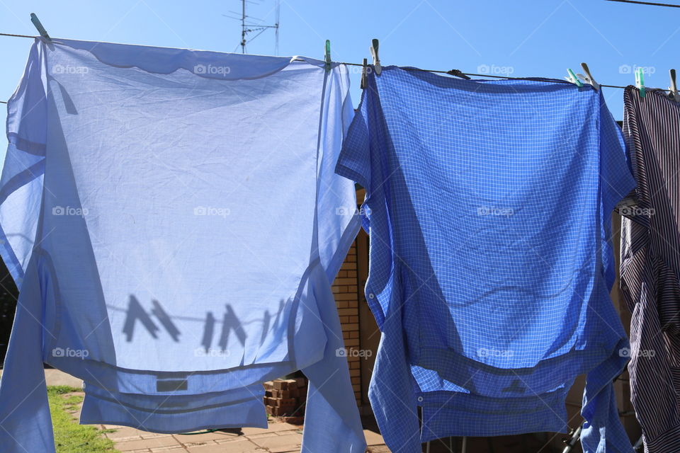 Clothesline and clothespin clothes pegs shadows through hanging laundry on outdoor laundry line on sunny day