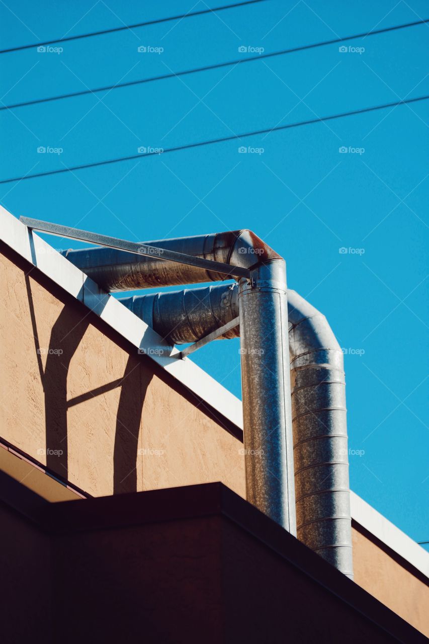 artistic shadowy modern shot of building with industrial metal vintage retro piped and blue sky yellow building aesthetic 