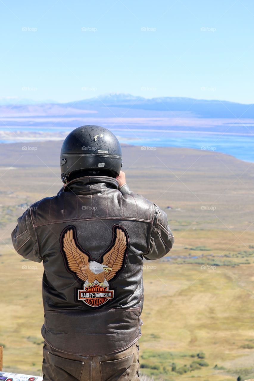 Motorcyclist wearing leather jacket and helmet st scenic lookout in Nevada overlooking Sierra Nevada mountains and lake in summer