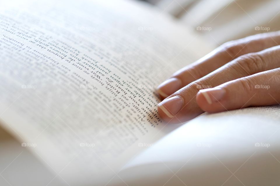 A portrait of someones hand lying in a book. the person is relaxing by reading some literature. the perfect leisure activity.