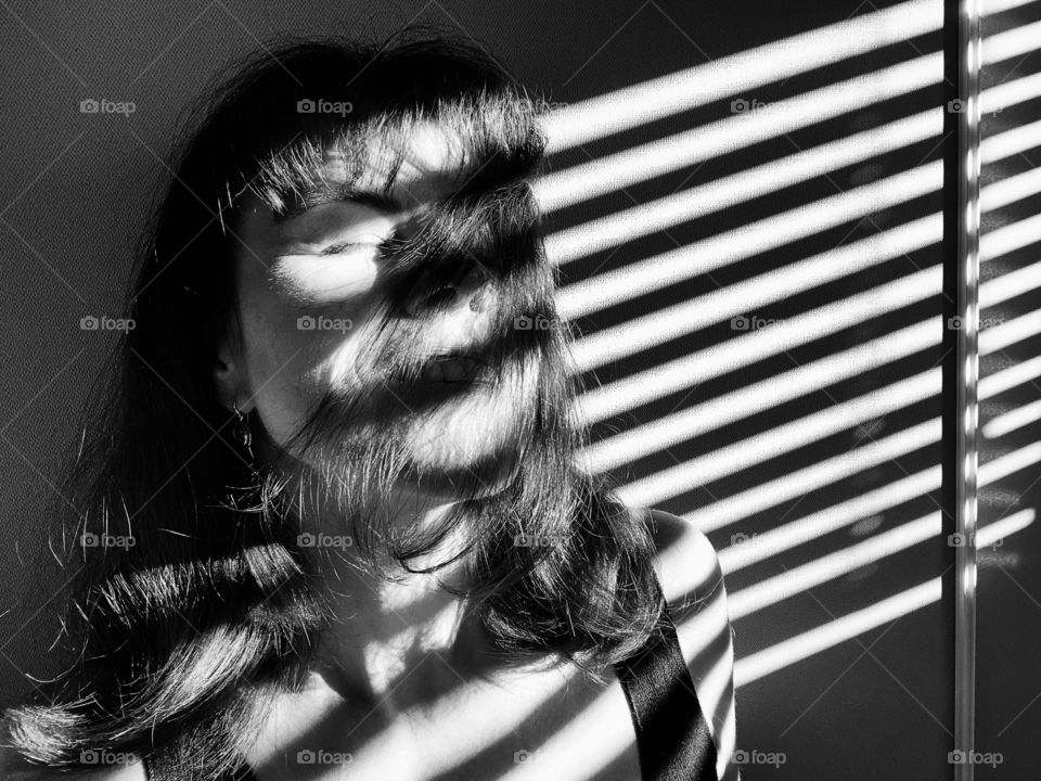 Black and white woman’s portrait in sunlight and shadow with long hair on her face