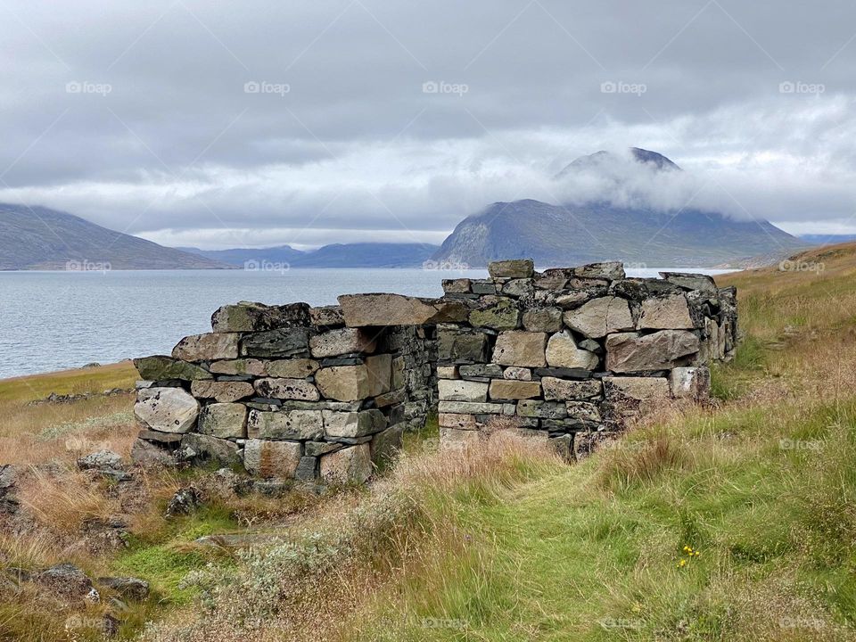 A grassy hill with the remains of a Viking village and mountains in the background