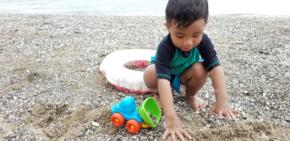 baby playing in the sand with toy truck
