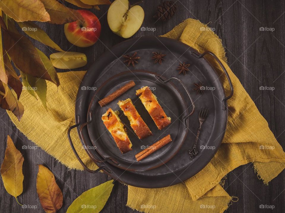 Three apple muffin slices in iron vintage plates lay on a black wooden table with a yellow kitchen napkin,apples and fall leaves,flat lay close-up.