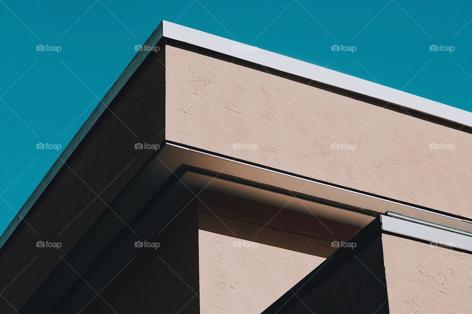 aesthetic modern building corner with deep shadows, bright pretty blue sky and tan building 
