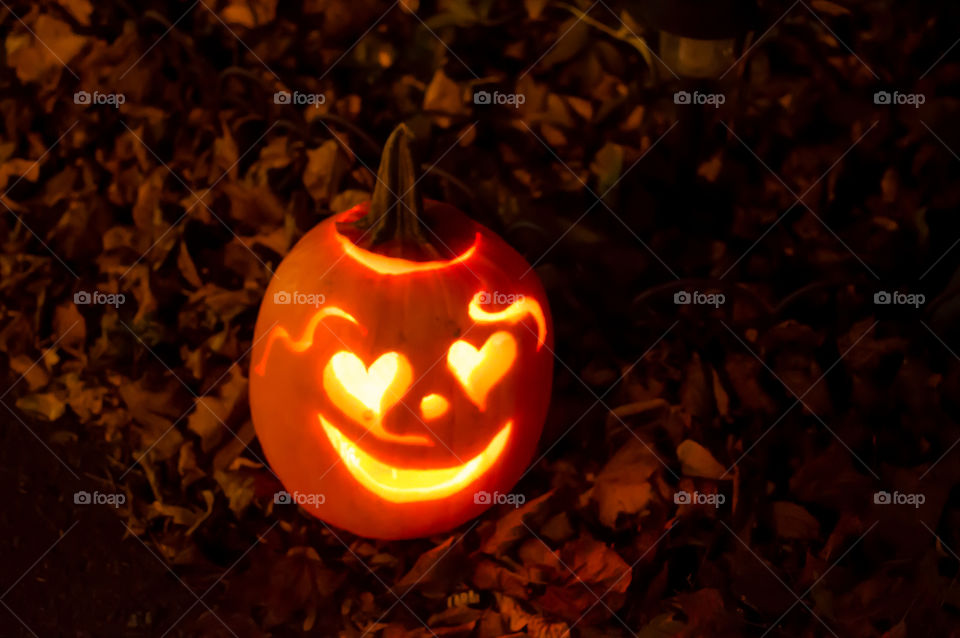 Heart shaped eyes on a happy pumpkin Jack o’lantern outdoors on autumn leaves welcoming Halloween treat or treating outdoor home decoration 