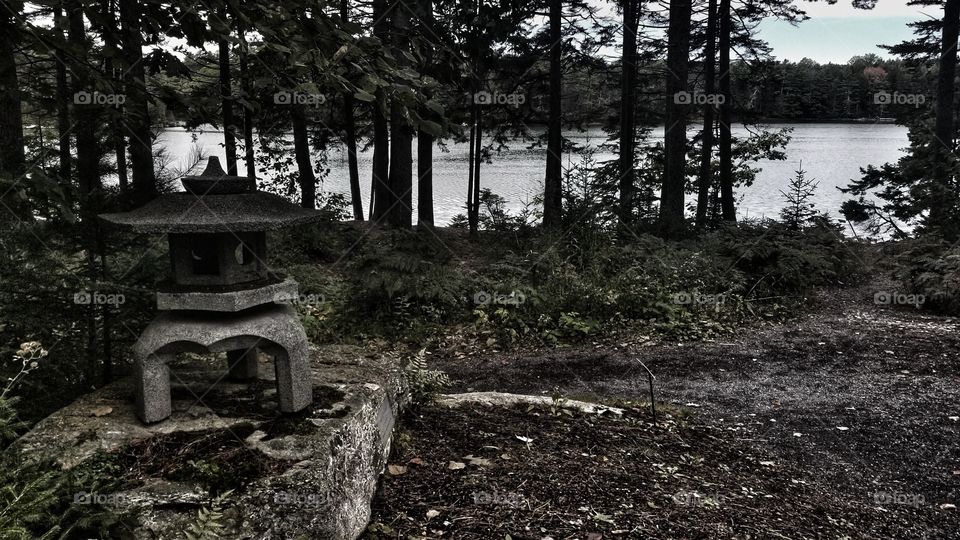 A moody picture of a rainy forest with a stone lantern on a river. Taken at the Coastal Maine Boatanical Gardens in Boothbay Maine.