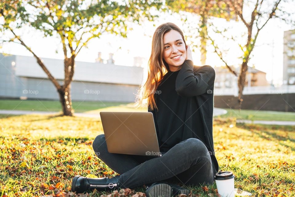 Young smiling brunette woman freelancer in casual working on laptop at city street