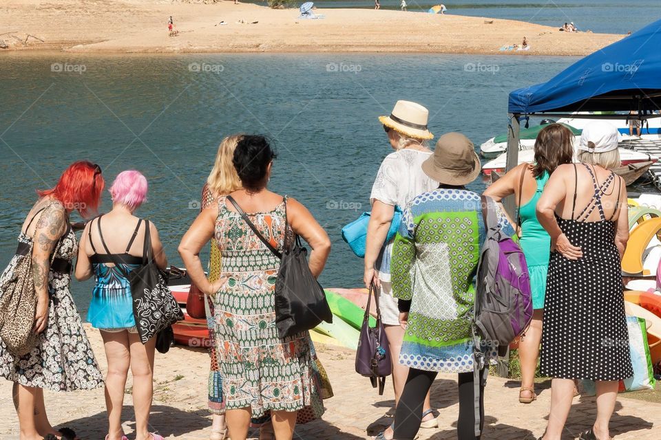 A group of mature and fabulous ladies dressed in summer clothes, await riverside to board a boat trip.