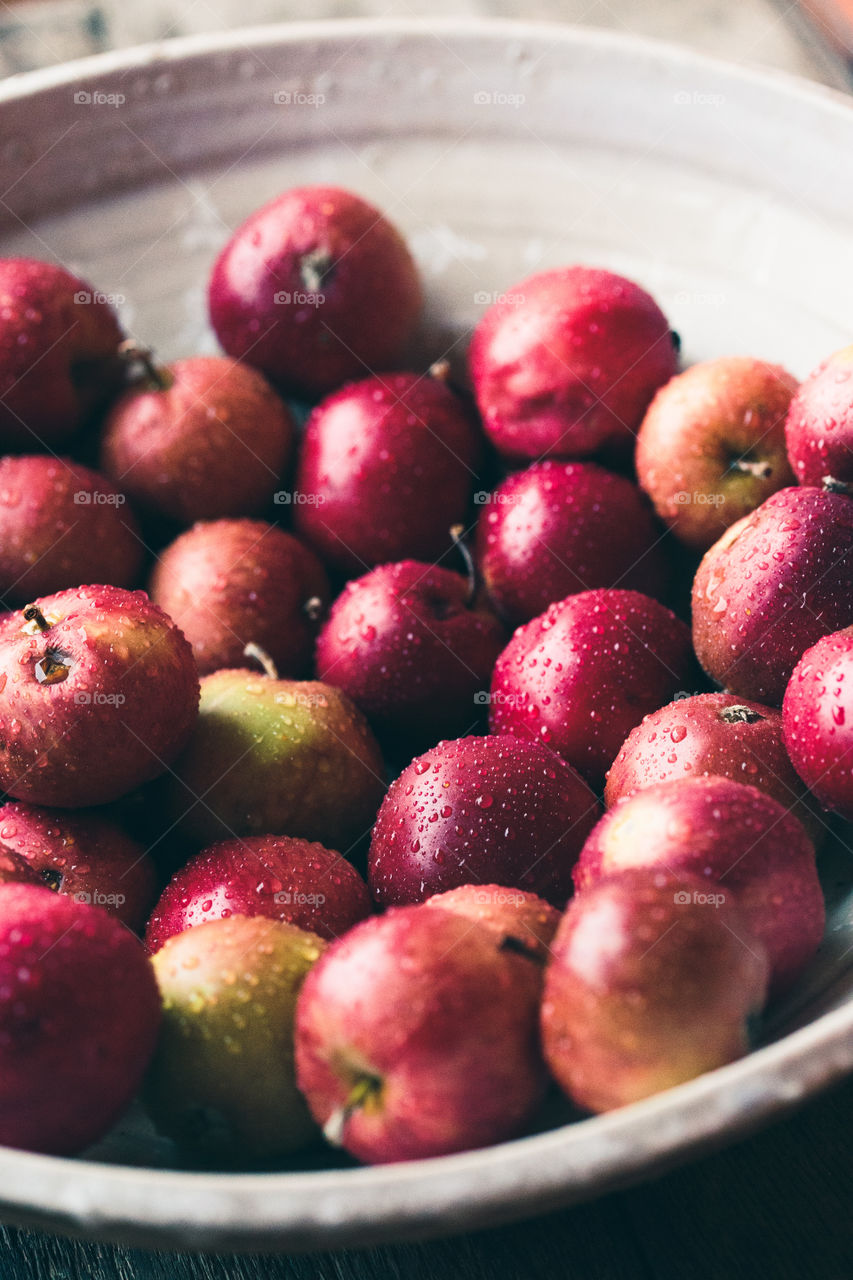 Closeup of big bowl of fresh red apples sprinkled raindrops on wooden table