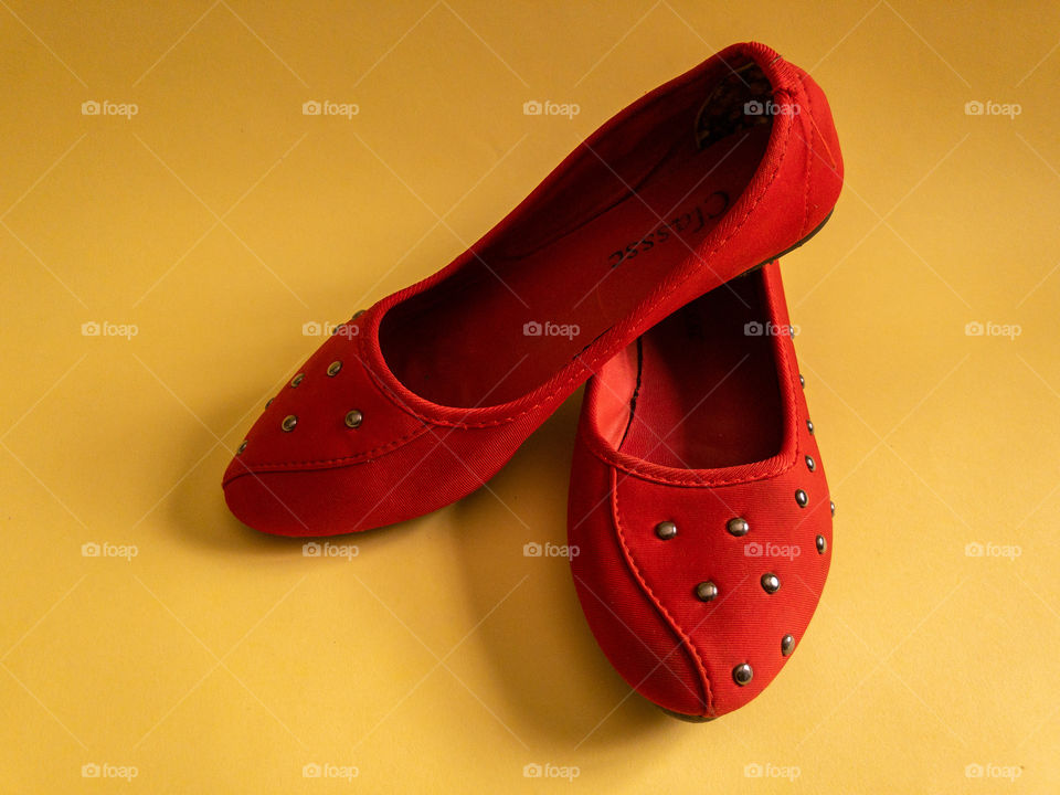 Pair of female red shoes on a yellow surface with metal designs on them and shadows underneath