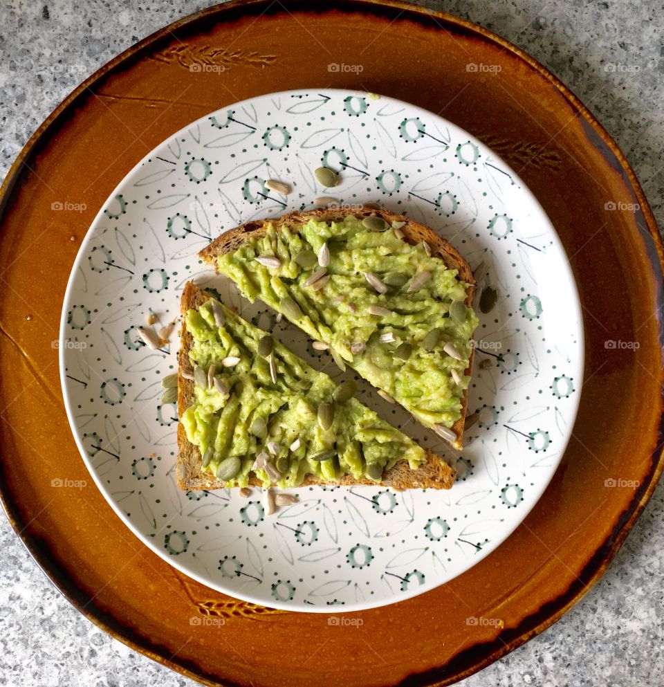 Avocado toast on seeded bread scattered with pumpkin and sunflower seeds and drizzled with olive oil