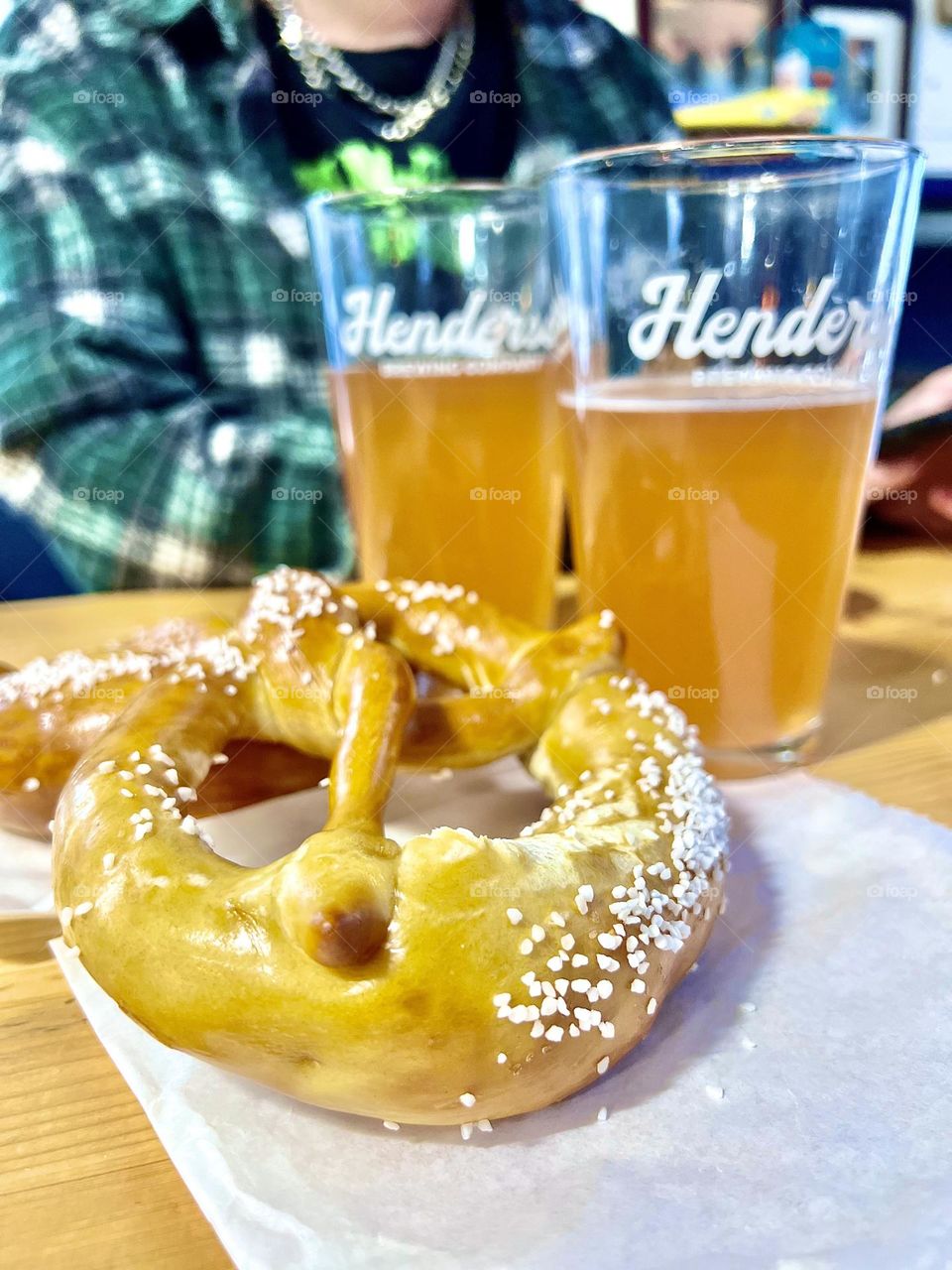 A large soft pretzel with a cold beer in the background 