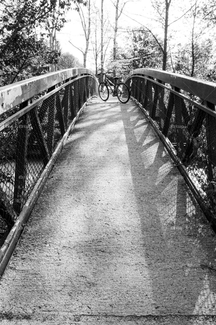 Lonely bicycle standing on its own on a bridge over a creek in the morning sunlight.