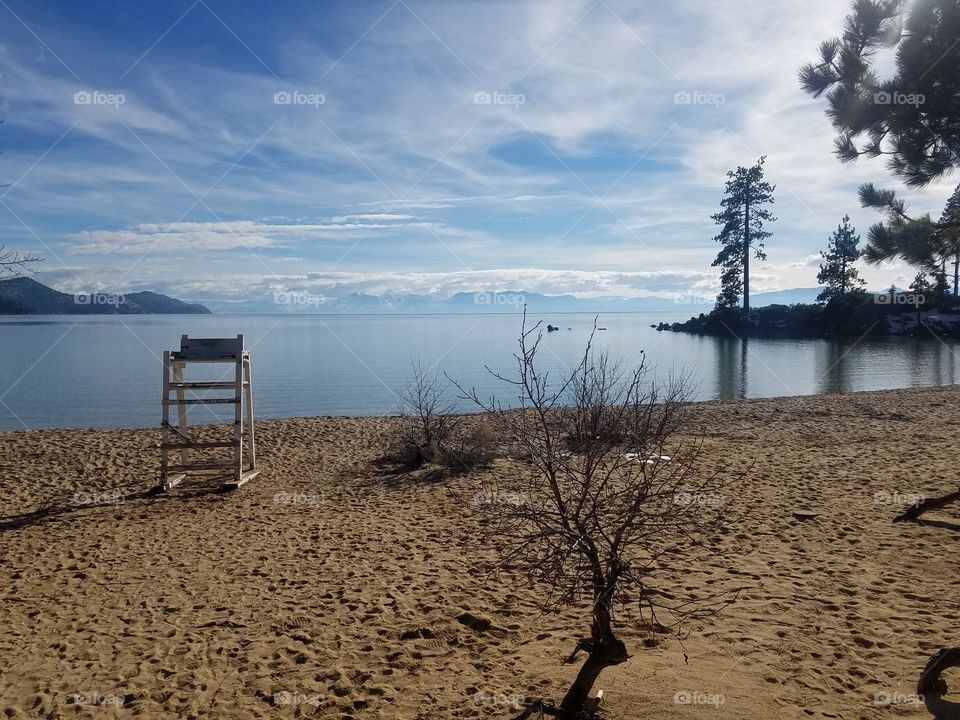 Empty Sand Harbor beach on Lake Tahoe in the wintertime with an empty lifeguard stand with snowy mountains in the background
