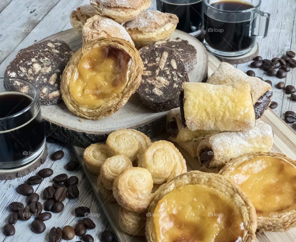 Coffee & assorted pastries on a pale wooden background 