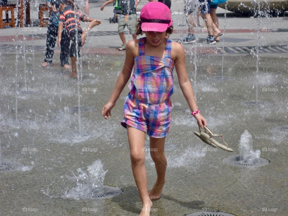 Girl having fun in city fountain on summer vacation