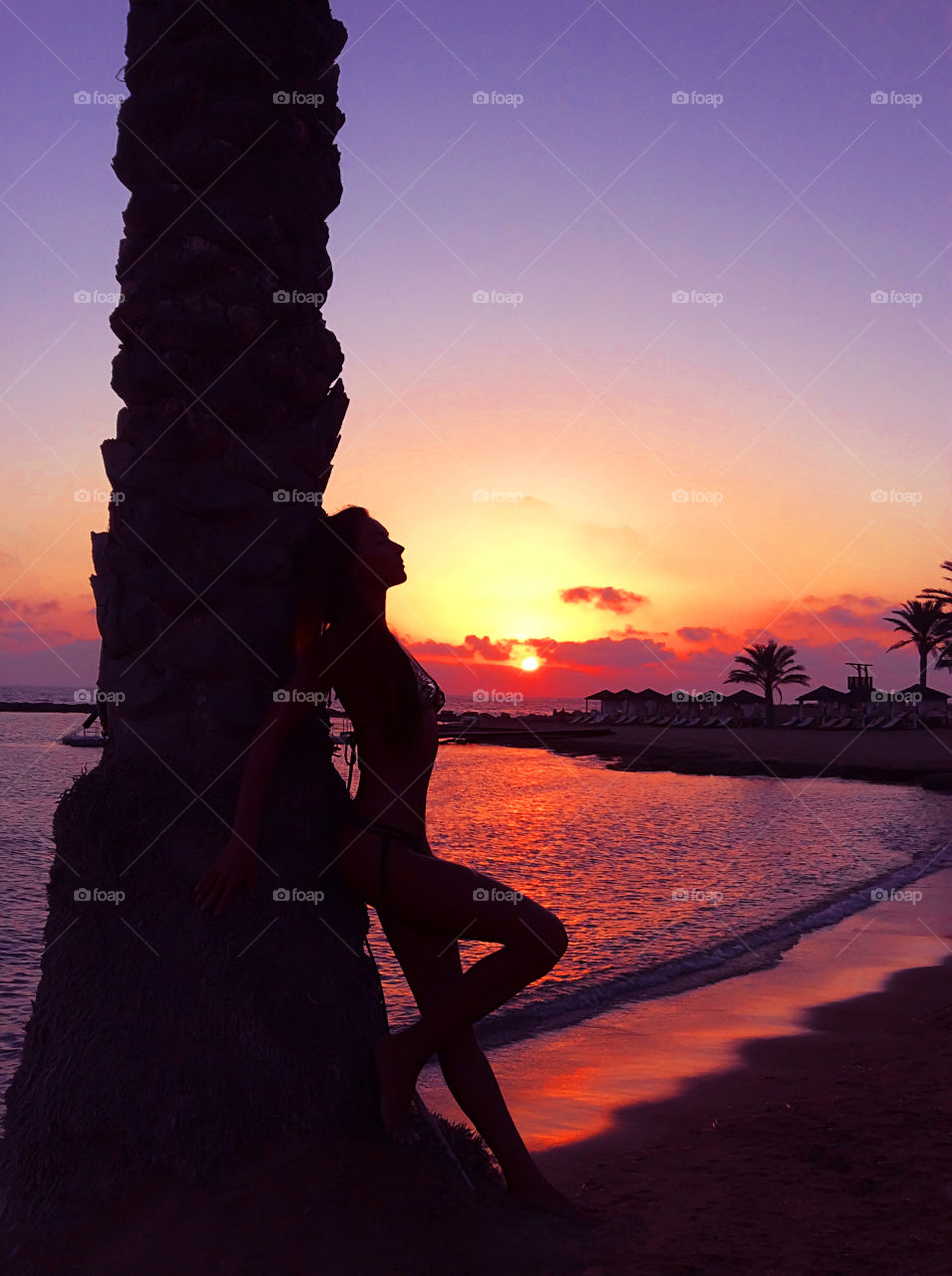 Silhouette of young woman nearby palm tree at the tropical beach on sunset background 