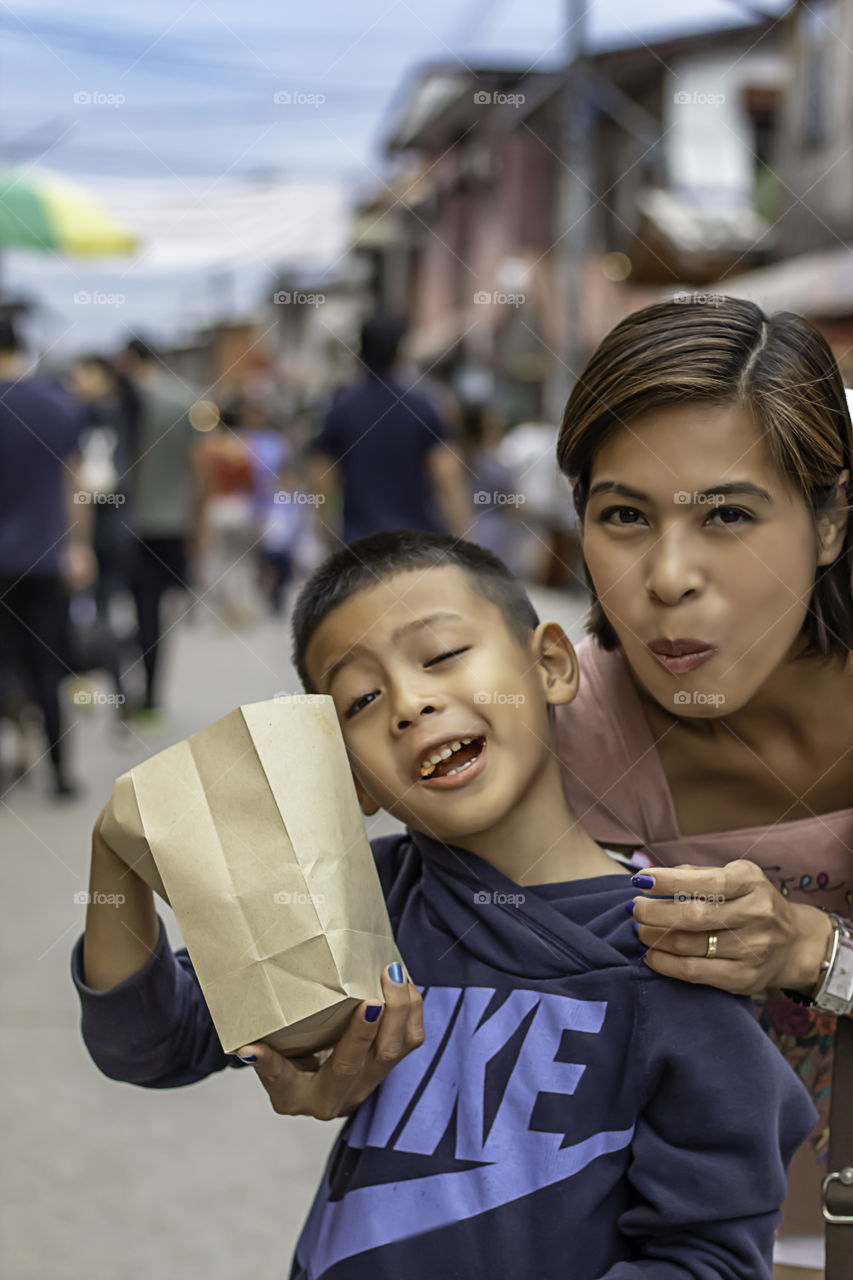 Mother and son eat candy on the street and blurry tourists at Walking Street Chiang Khan, Loei in Thailand.