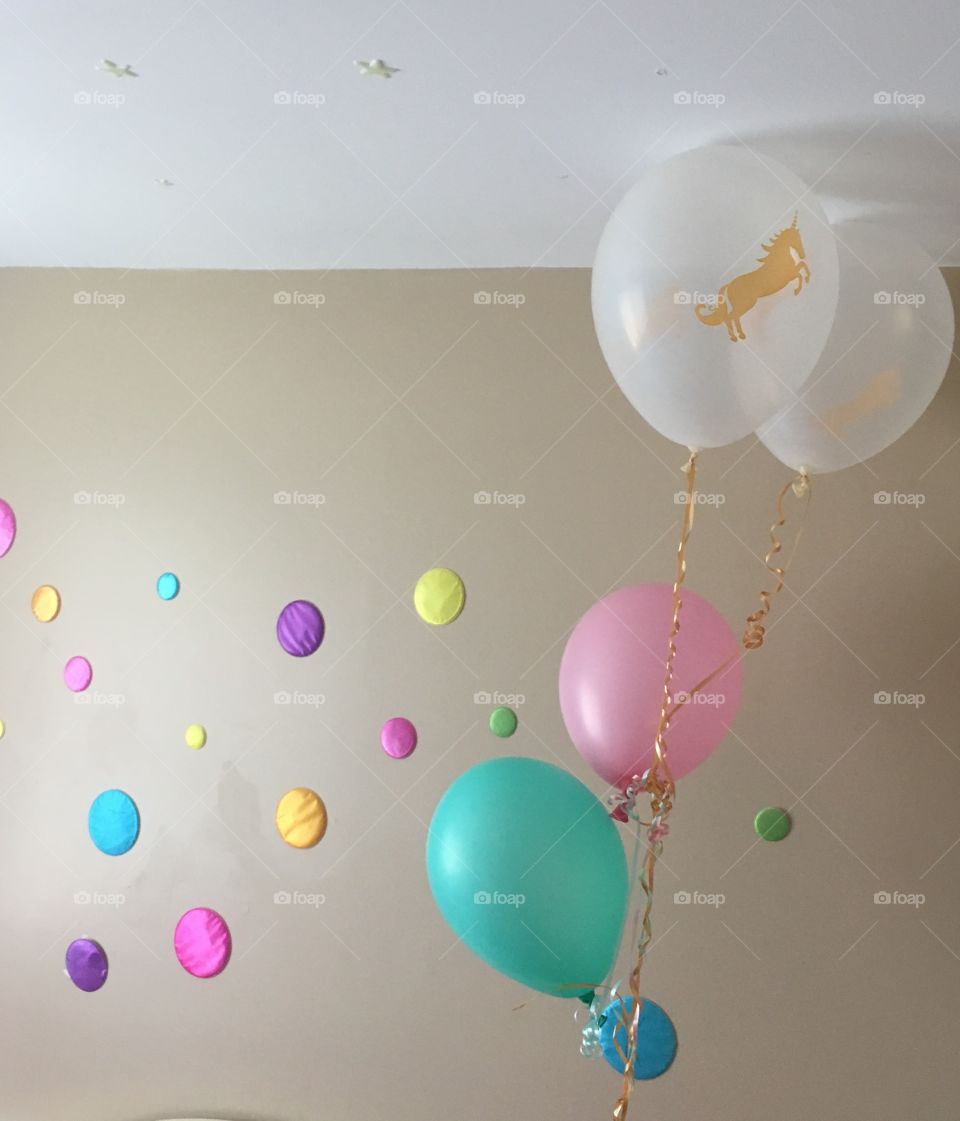 Little girl’s Unicorn party room. Soft pastel coloured balloons, white, pink, teal with gold unicorn and rainbow of polka dots on wall. 